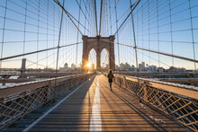 Woman Walking Across The Brooklyn Bridge At Sunrise, New York City, USA