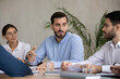 © fizkes - Confident 30s bearded businessman talking at meeting with multiracial young partners in office. Motivated focused diverse teammates listening to male european colleague, brainstorming indoors.