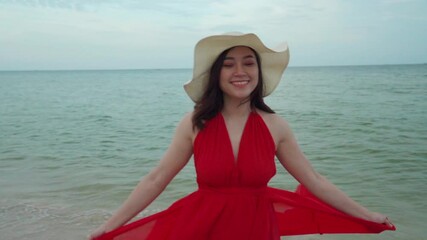 Wall Mural - slow-motion of woman with arms spread in a red dress on the sea beach with wind blow