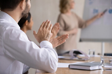 Close up happy young businessman clapping hands with mixed race colleagues, thanking older mature female speaker for educational lecture seminar workshop in modern office, appreciation concept.