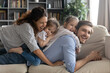 © fizkes - Smiling bonding full family lying on comfortable couch, enjoying playtime together at home. Happy affectionate couple parents spending lazy weekend holiday time with little preschool baby daughters.