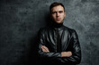 © amixstudio - Caucasian unshaven sexy male model with brutal serious face in black leather jacket with crossed arms looking at camera on dark background isolated