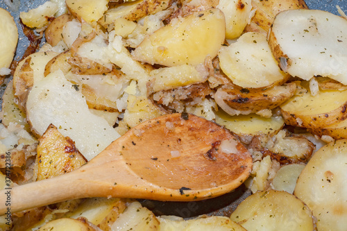 Hot baked potato slices with thin skinned potatoes on a plate with a wooden spoon. A simple and quick after-work meal for the worker and bachelor. Inexpensive food for poor people and farmers