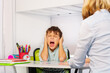 Autistic boy scream and close ears in pain during ABA development therapy sitting by the table with teacher