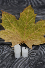 Two candlesticks on brushed pine boards. Nearby is a dried maple leaf.