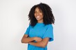 © Roquillo - Young african woman with curly hair wearing casual blue shirt over white background happy face smiling with crossed arms looking at the camera. Positive person.
