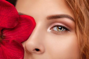 Eyes and eyebrows close up. Portrait of a beautiful teenage girl with beautiful makeup and healthy clean skin. Near the face is red orchid flower. Makeup and cosmetology concept.