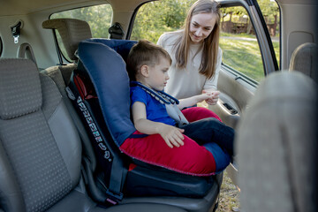 Mother gives the phone little boy sitting in a car seat. Safety of transportation of children.