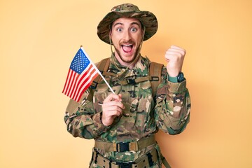 Canvas Print - Young caucasian man wearing camouflage army uniform holding usa flag screaming proud, celebrating victory and success very excited with raised arms