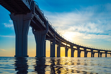 Wall Mural - Road bridge at sunset. Two-level bridge over the water. Highway over the Bay. The highway passes over the river. A long bridge over the water and the setting sun.