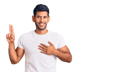 Young latin man wearing casual clothes smiling swearing with hand on chest and fingers up, making a loyalty promise oath