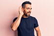 © Krakenimages.com - Young hispanic man wearing casual clothes smiling with hand over ear listening and hearing to rumor or gossip. deafness concept.