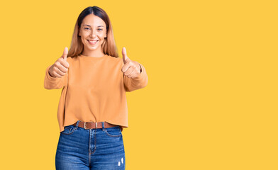 Beautiful young woman wearing casual clothes approving doing positive gesture with hand, thumbs up smiling and happy for success. winner gesture.