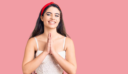 Brunette teenager girl wearing elegant look praying with hands together asking for forgiveness smiling confident.