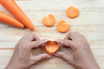 Wall Mural - Heart crafting on the carrot with hands pressing. heart shaped aluminium vegetables stamp