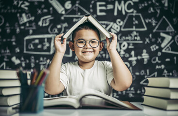 Wall Mural - A boy with glasses studied and put a book on his head in the classroom.