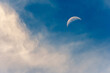 Crescent moon against a blue daytime sky with soft clouds around the moon. 