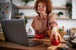 © JustLife - Young woman is reading a recipe while cooking. Beautiful woman with curly hair enjoying in the kitchen.