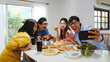 © tirachard - Happy young group having lunch at home. Asia family party eating pizza food and making selfie with her friends at birthday party at dining table together at house. Celebration holiday and togetherness