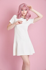 Beautiful girl with pink hair, hair coloring. Cute anime woman stands on a pink background in a short white dress. Colored hair, perfect hairstyle