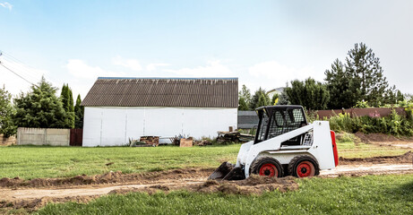 Wall Mural - A skid steer loader clears the site for construction. Land work by the territory improvement. Machine for work in confined areas. Small tractor with a bucket for moving soil and bulk materials.