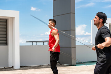 Wall Mural - Two handsome Caucasian sportsmen doing morning outdoor exercise jump rope on building rooftop