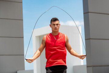 Wall Mural - Handsome Caucasian athlete doing morning outdoor exercise jump rope on building rooftop