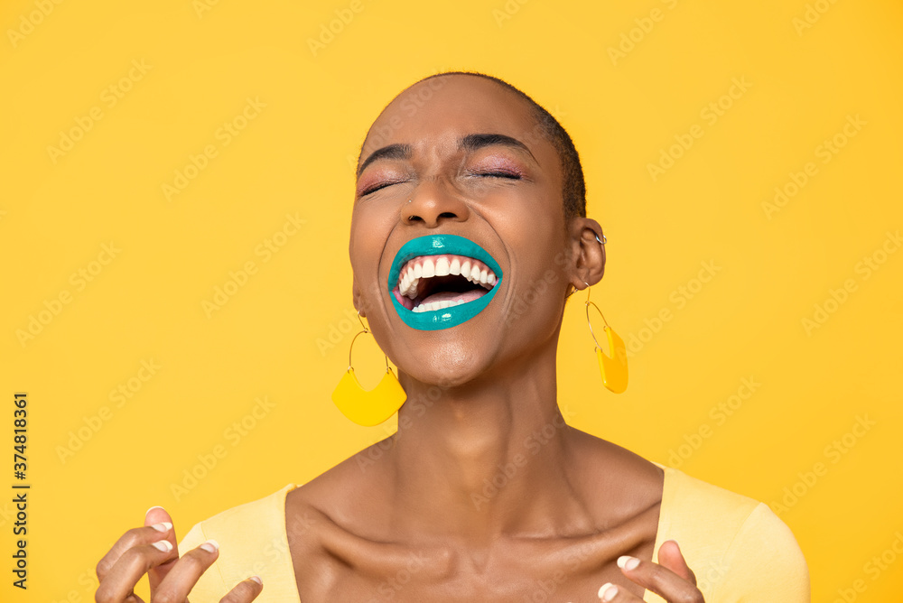 Close up portrait of laughing young African American woman with fashionable colorful make up isolated on yellow studio background - obrazy, fototapety, plakaty 