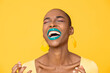 Leinwandbild Motiv Close up portrait of laughing young African American woman with fashionable colorful make up isolated on yellow studio background