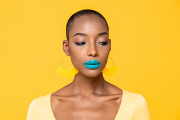 Wall Mural - Close up portrait of upset young African American woman with fashionable colorful make up looking down isolated on yellow studio background