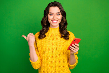Wall Mural - Portrait of positive cheerful girl use smart phone point forefinger copyspace present online ads promo wear style stylish sweater isolated over bright shine color background