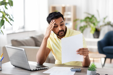 Poster - remote job, technology and people concept - stressed young indian man with calculator and papers working at home office