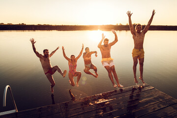 Group of young friends having fun enjoying a summer day swimming and jumping at the lake.