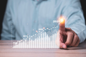 Businessman  pointing to virtual investment bar and line graph on wooden table as business strategy and stock value investor concept.