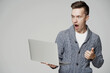© muse studio - surprised young man of Caucasian appearance, looks at the laptop. emotion on the face of joy, open mouth. stylish brunette hairstyle. he's wearing a gray sweatshirt. gray background