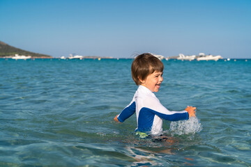 Happy little child having fun playing in sea water. Summer holidays lifestyle, carefree childhood. Sun protection swimwear.