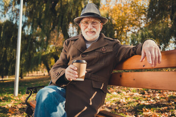 Canvas Print - Photo of positive old man rest relax october fall weekend park pause sit bench enjoy aromatic takeaway coffee mug wear cap headwear jacket