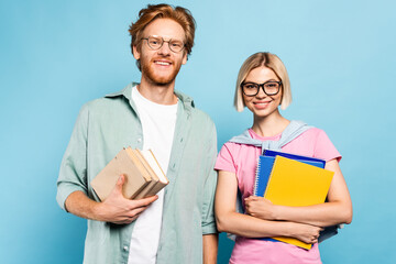 young students in glasses holding notebooks and books while standing on blue