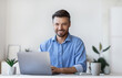 © Prostock-studio - Smiling Young Businessman Sitting At Desk With Laptop In Modern Office