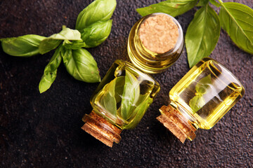 Wall Mural - A transparent glass bottle of basil essential oil with fresh basil leaves on rustic table