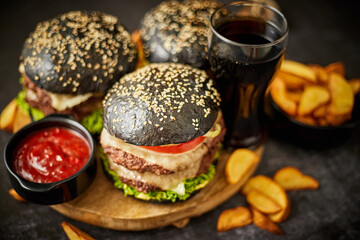 Homemade delicious black burgers served on wooden cutting board with ketchup, potato wedges