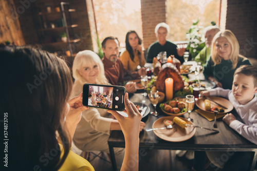Photo of full family gathering eight people little photographer daughter hold telephone make portrait memorize moment dinner big table turkey generation in home evening living room indoors