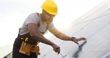 Portrait Of African American Engineer In Safety Helmet And Uniform At Solar Power Station Installing Solar Panels. Green Energy.