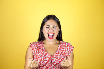 Young beautiful woman over isolated yellow background very happy and excited making winner gesture with raised arms, smiling and screaming for success.