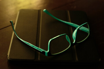 Blue eye glasses and android tablet on wooden brown table.