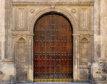 Ancient Door In The Old Town With A Wooden Gate, Stone Semicircular Arch With Ornaments In The Facade Around The Entrance Of A Medieval Palace Or A Church
