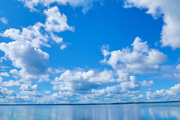 clouds and blue sky above the water of lake, river or sea bay and far bank or shore with forest on t