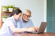 © PinkBlue - Nurse help senior retirement man working with laptop at home and feeling happy