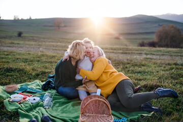 Small girl with mother and grandmother having picnic in nature at sunset.