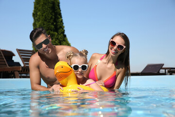 Wall Mural - Happy family with inflatable ring in outdoor swimming pool on sunny summer day